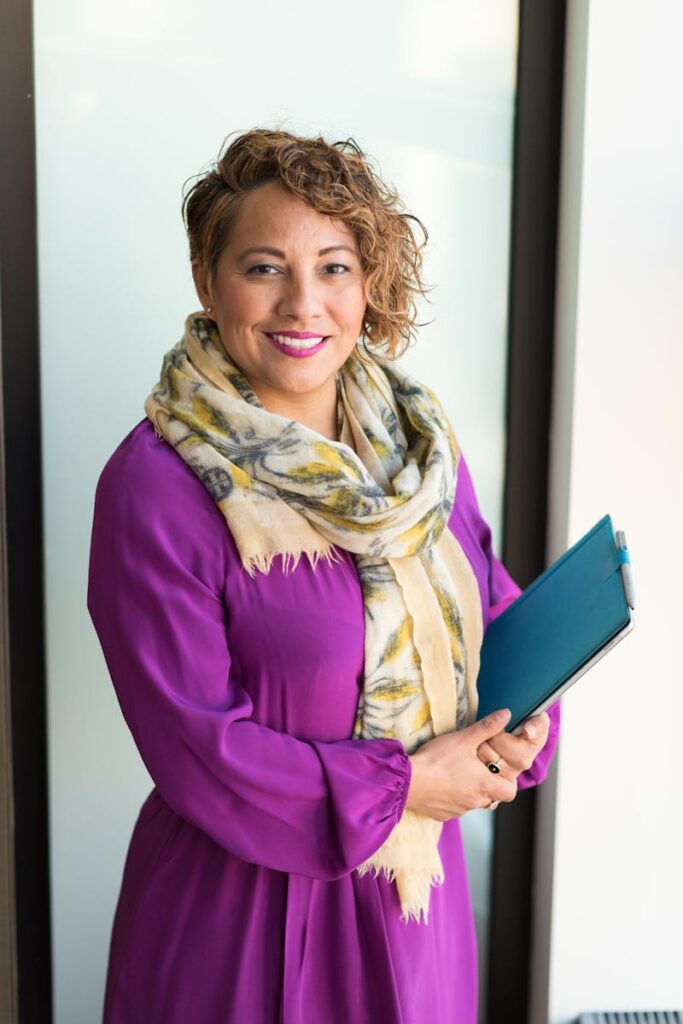 Smiling woman in a purple dress and scarf holding a tablet indoors.